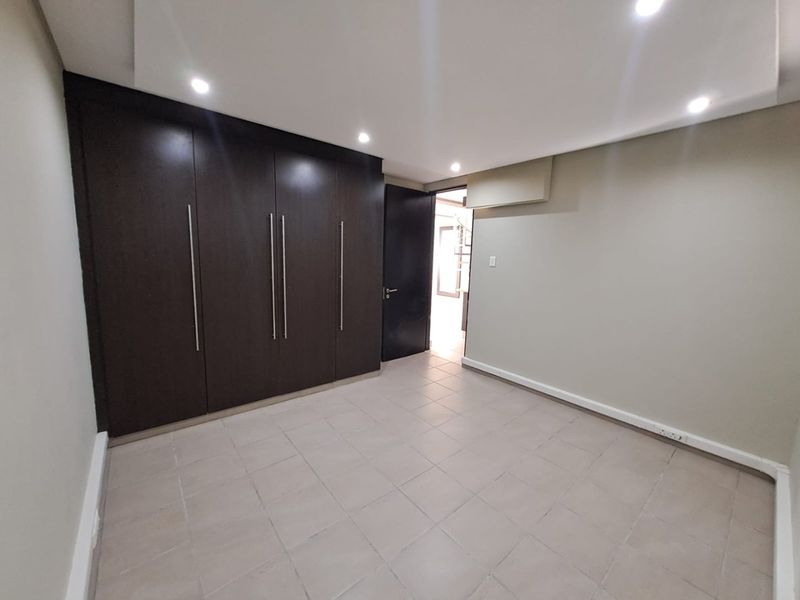 An empty bedroom featuring tiled flooring, built-in dark wood cupboards, recessed ceiling lighting, and a wall-mounted air conditioning unit.