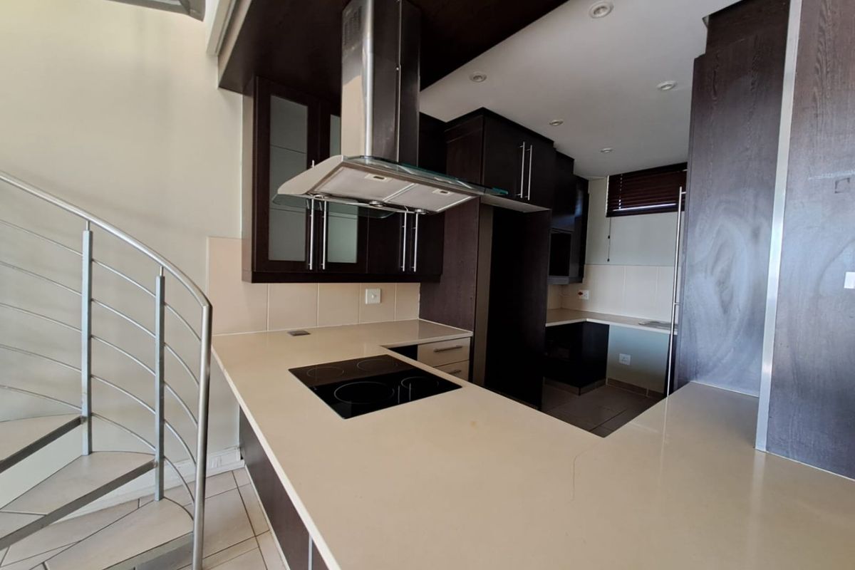 Modern kitchen featuring dark cabinetry, stone countertops, integrated electric hob, and a striking spiral staircase leading to the upper level.