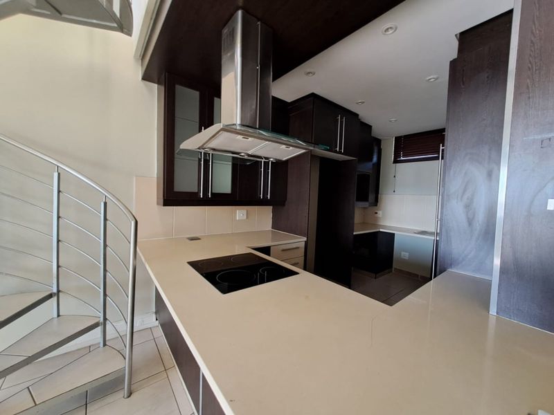 Modern kitchen featuring dark cabinetry, stone countertops, integrated electric hob, and a striking spiral staircase leading to the upper level.