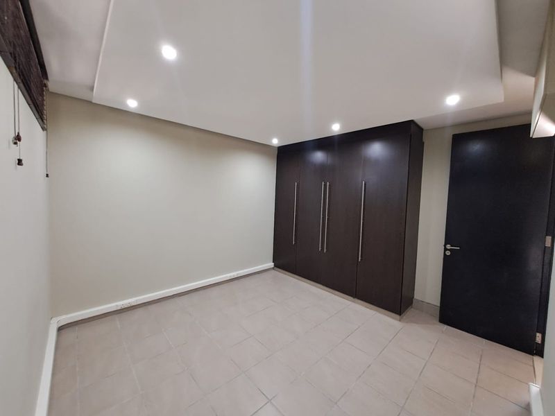 A clean, empty bedroom featuring neutral tiled flooring, recessed ceiling lighting, and dark wood built-in cupboards.