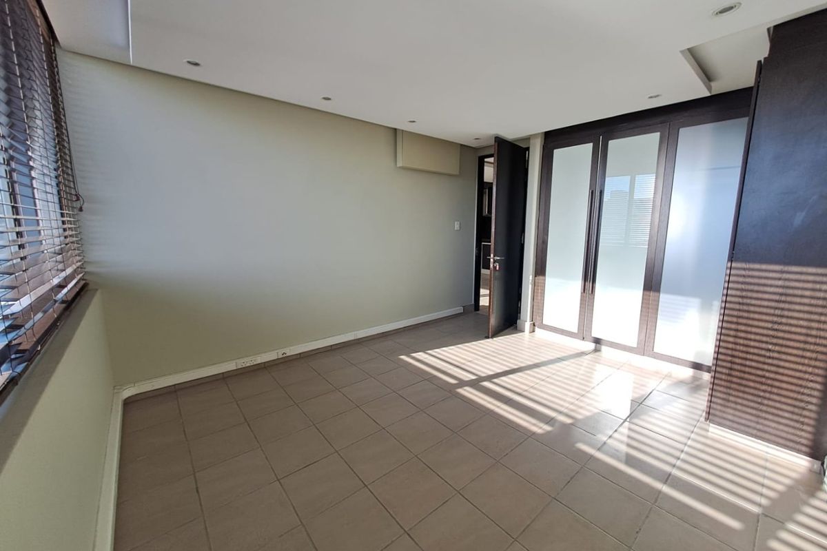 A spacious, empty bedroom featuring tiled flooring, recessed downlighting, and large built-in cupboards with frosted glass panels.