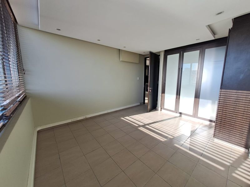 A spacious, empty bedroom featuring tiled flooring, recessed downlighting, and large built-in cupboards with frosted glass panels.