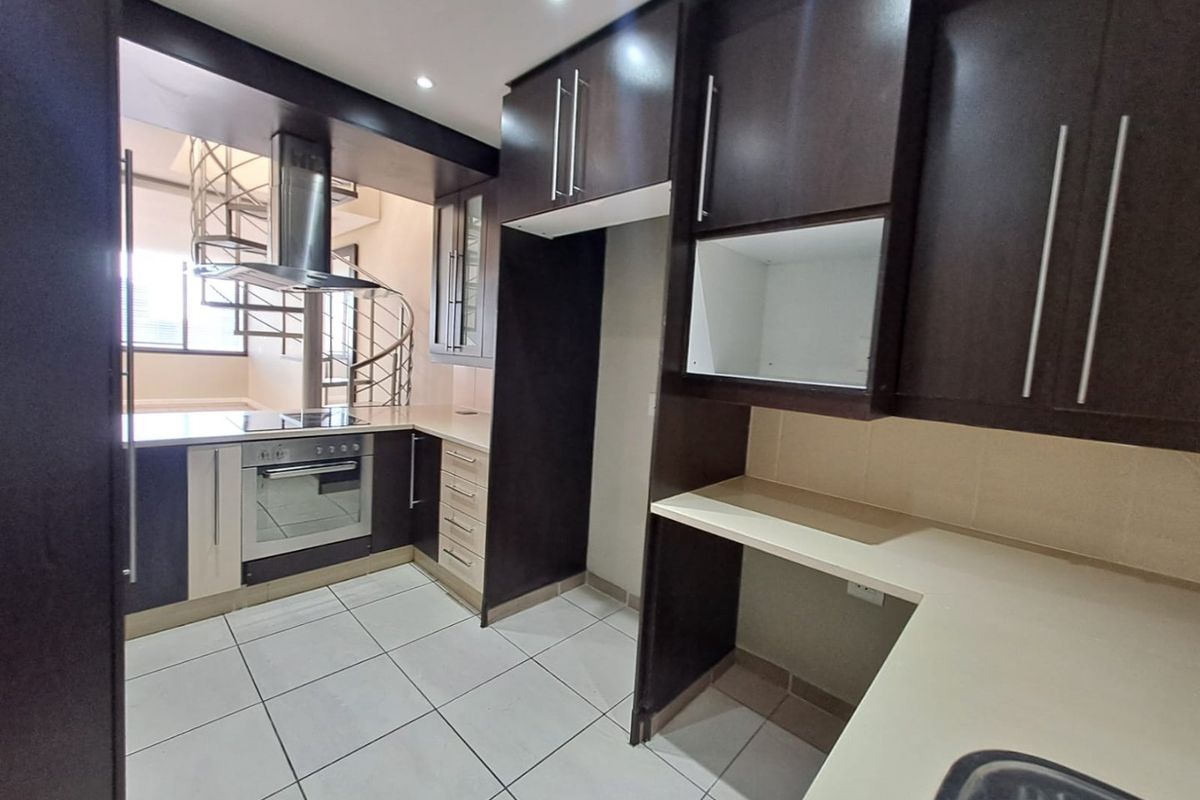 Modern kitchen featuring dark cabinetry, built-in oven and hob, extractor fan, and tiled flooring, with an adjacent spiral staircase.