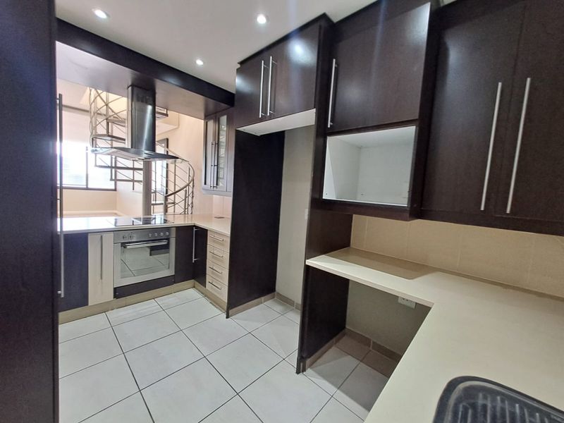 Modern kitchen featuring dark cabinetry, built-in oven and hob, extractor fan, and tiled flooring, with an adjacent spiral staircase.