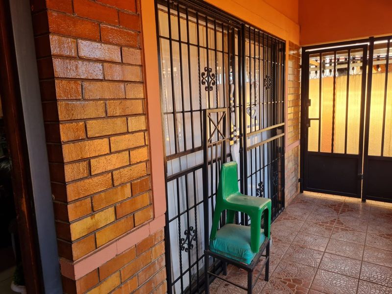 A covered patio area featuring brick wall finishes, tiled flooring, and secure metal security gates providing access to the home.