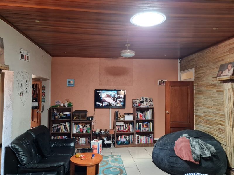 Living room featuring a timber-clad ceiling, stone accent wall, and tiled flooring, with a central skylight providing natural illumination.