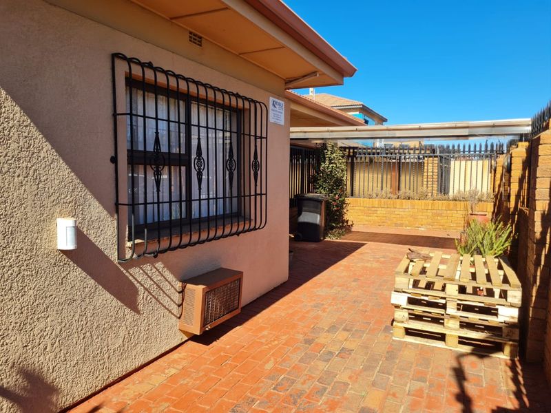 A paved rear courtyard area featuring a brick boundary wall, security bars on the window, and an external air conditioning unit.