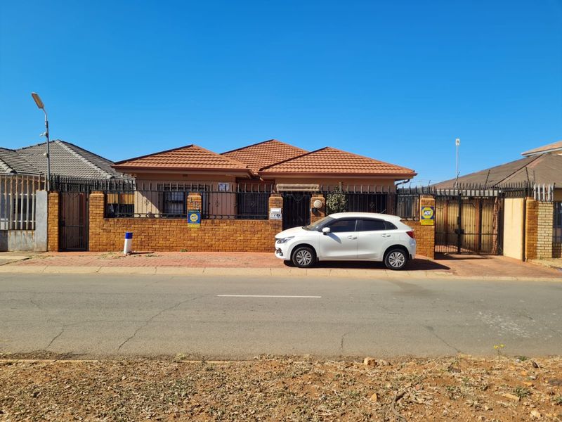 Front elevation of a single-story residential house featuring a tiled roof, brick boundary wall, and secure gated entrance.