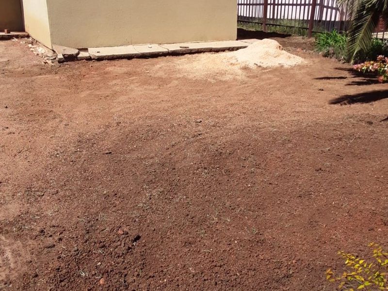 Rear yard area featuring bare soil, metal perimeter fencing, and a concrete foundation edge, offering potential for landscaping and garden development.