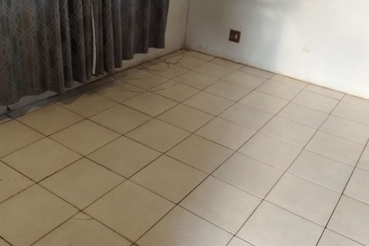 An empty living area featuring tiled flooring and neutral walls, requiring minor cosmetic updates and cleaning to restore its appeal.