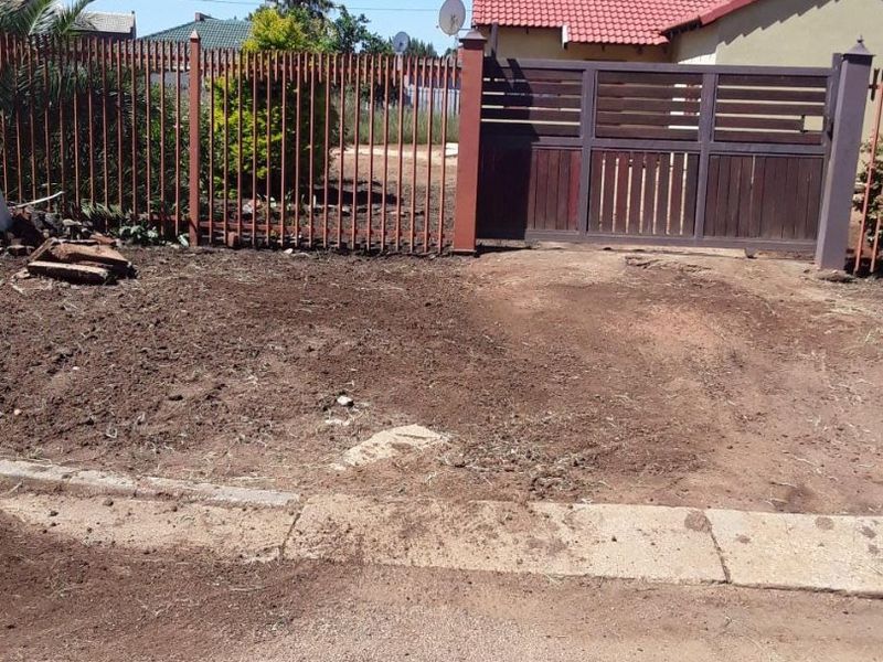 Front exterior view showing a sliding driveway gate, metal perimeter fencing, and an unpaved driveway area leading to the property.