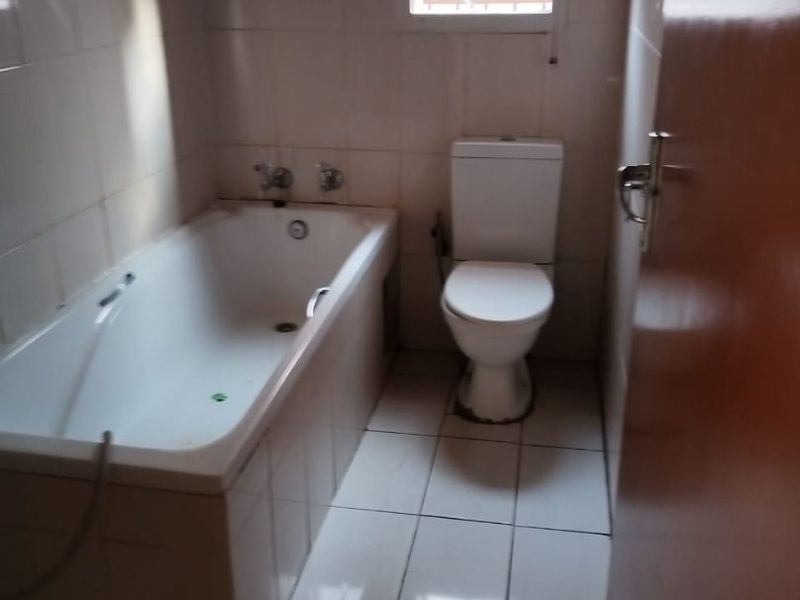 A functional bathroom featuring a built-in bathtub, toilet, and neutral tiled finishes throughout, offering a clean and practical space.