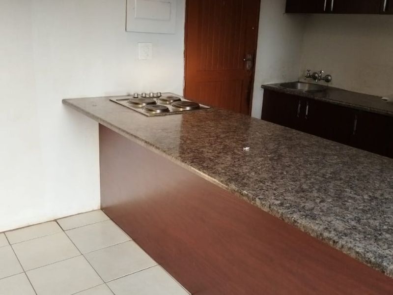 A functional kitchen featuring a granite breakfast bar with an integrated hob, dark cabinetry, and tiled flooring, ready for a modern update.