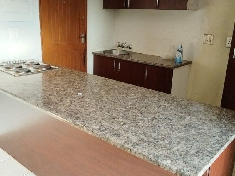 A functional kitchen area featuring a granite breakfast bar, built-in cabinetry, and an integrated electric hob, requiring minor cosmetic finishing to complete the space.