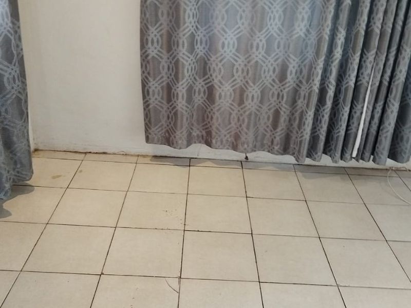 A close-up view of tiled flooring showing visible cracks and grout wear, with curtains visible in the background.