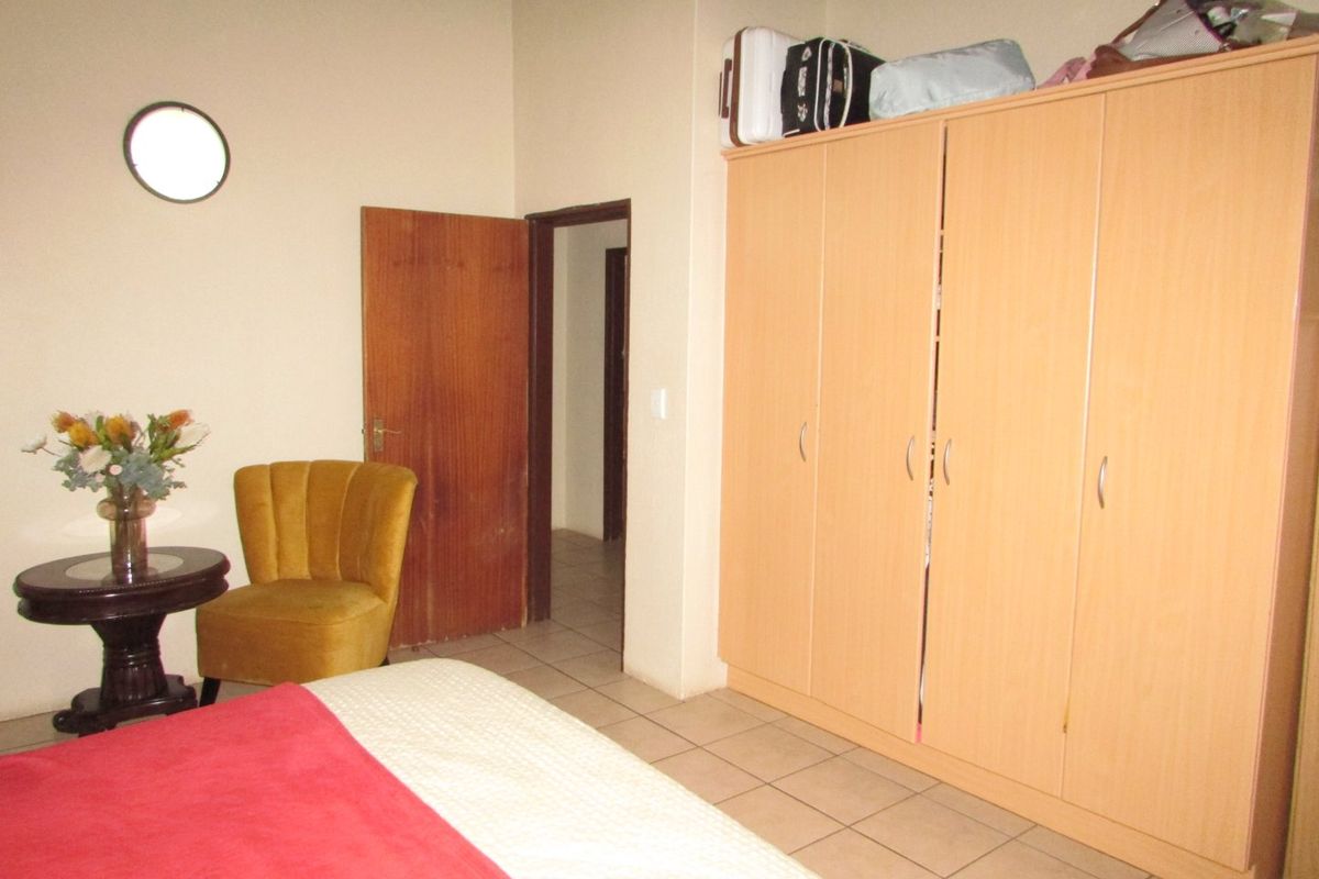A functional bedroom featuring tiled flooring, a built-in wardrobe, and a solid wood door, offering a practical layout for comfortable living.