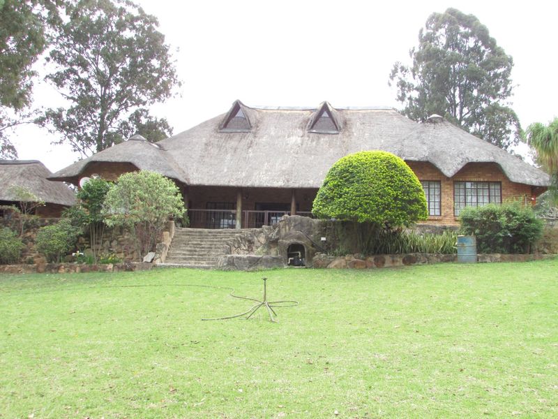 Rear view of a traditional farmhouse featuring a thatched roof, dormer windows, and a stone-walled garden with a staircase leading to a covered patio.