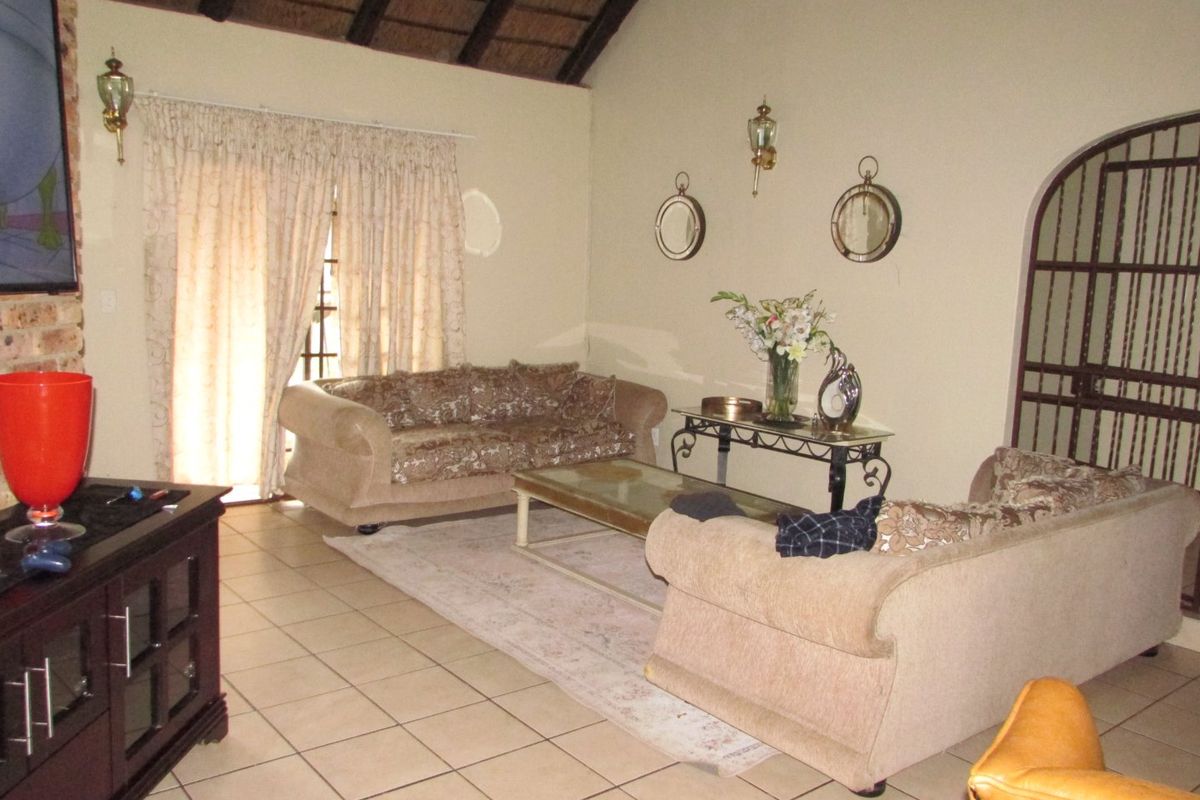 Spacious living room featuring tiled flooring, an exposed thatch ceiling, and an arched security gate, offering a rustic farm-style aesthetic.