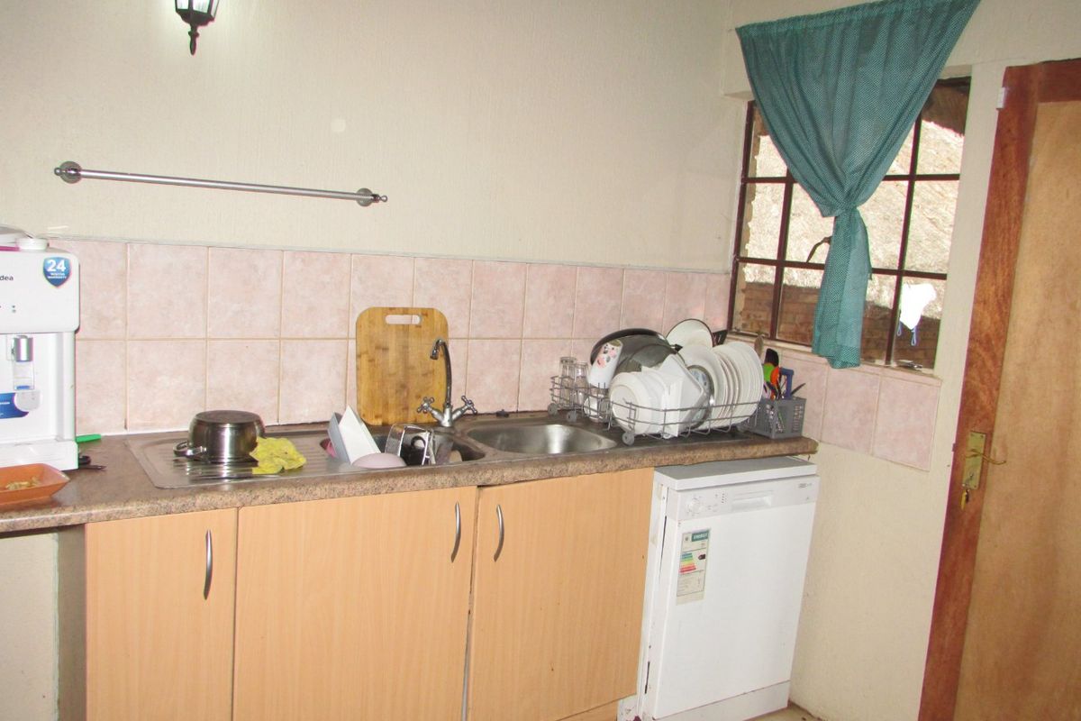 A compact kitchen area featuring laminate cabinetry, a stainless steel sink, tiled backsplash, and tiled flooring, requiring cosmetic updates to modernize the space.