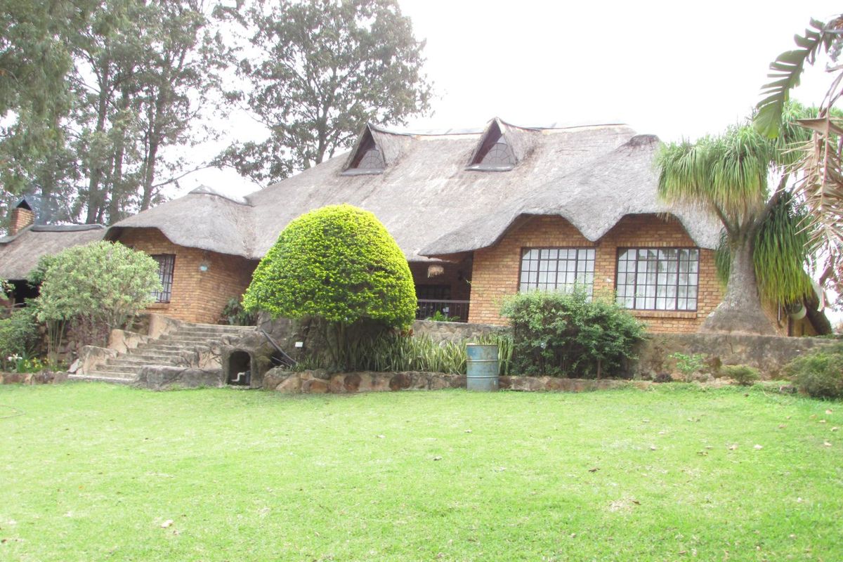 Rear view of a traditional farmhouse featuring a thatched roof, brick exterior, and stone landscaping elements set within a spacious garden.