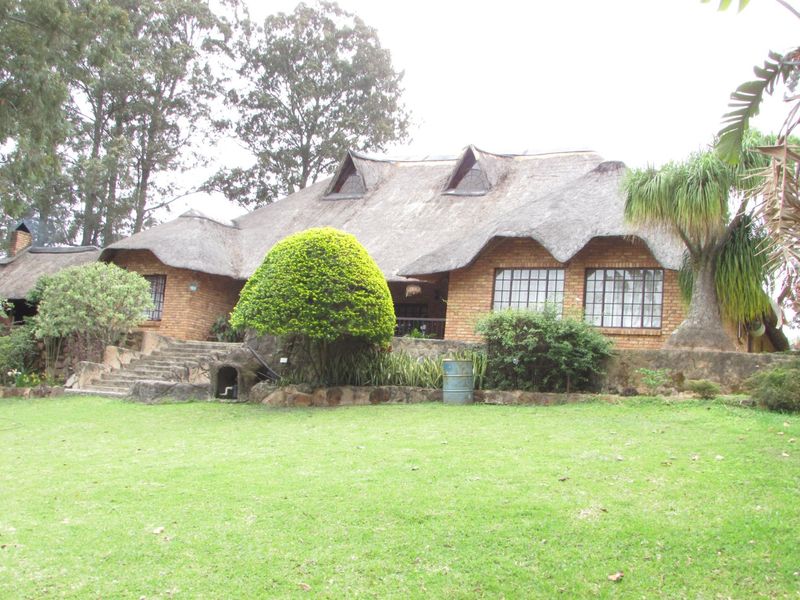 Rear view of a traditional farmhouse featuring a thatched roof, brick exterior, and stone landscaping elements set within a spacious garden.