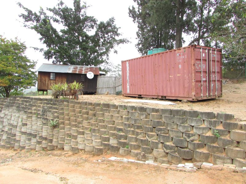 Exterior view of a farm property featuring a timber structure with a corrugated roof, a large shipping container, and a concrete block retaining wall.