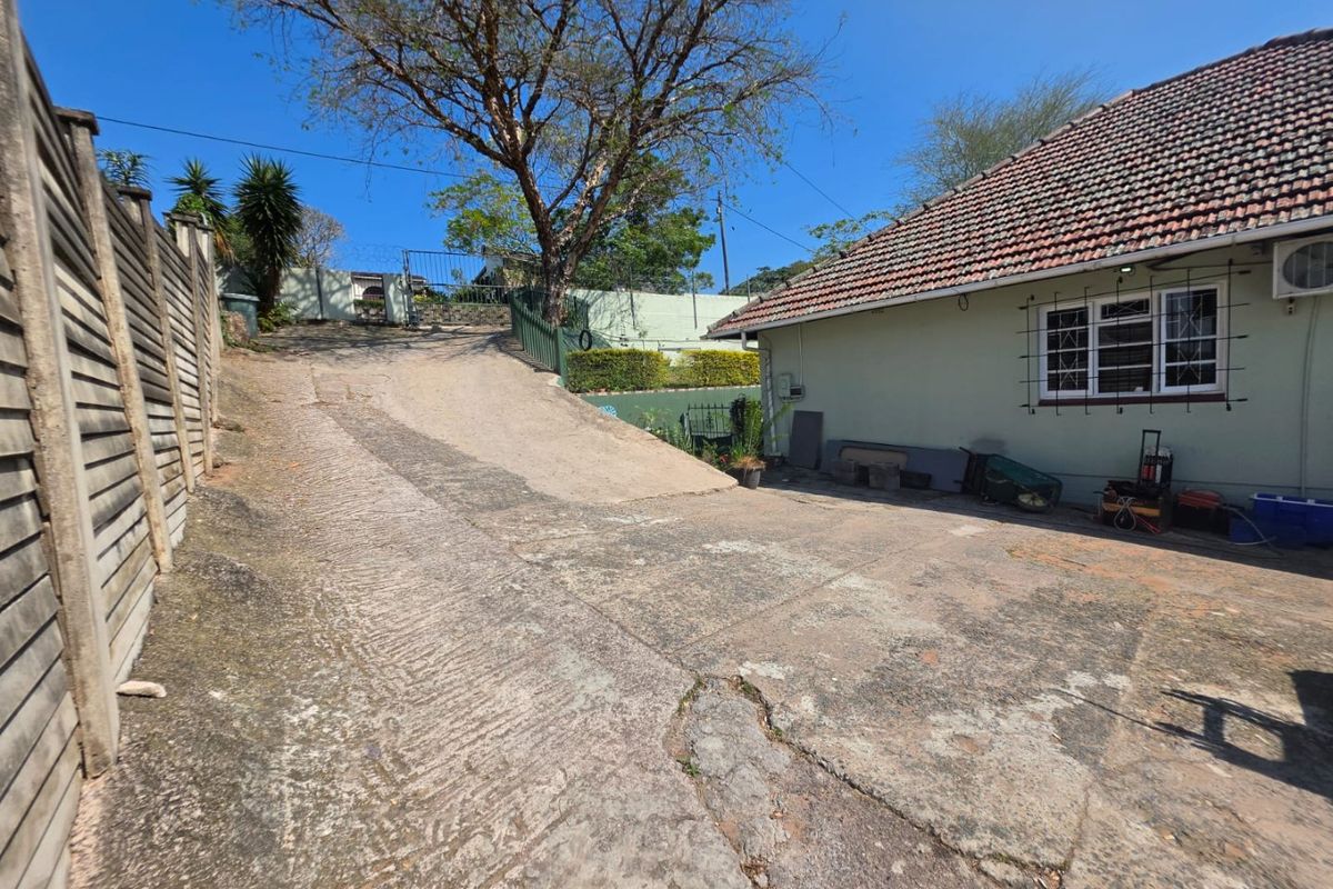 Exterior view of the rear property featuring a concrete driveway, tiled roof, and perimeter fencing with security bars on the windows.