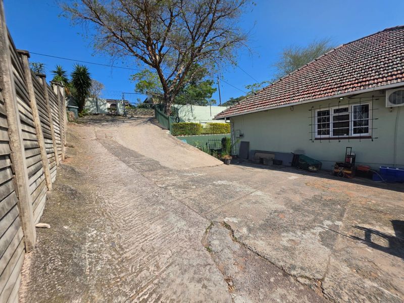 Exterior view of the rear property featuring a concrete driveway, tiled roof, and perimeter fencing with security bars on the windows.
