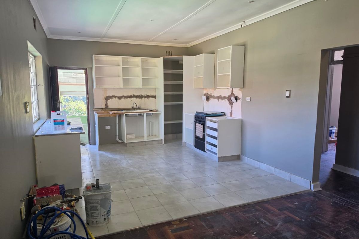 An unfinished kitchen area featuring tiled flooring, built-in cabinetry, and a freestanding stove, currently undergoing renovation with exposed wall sections.