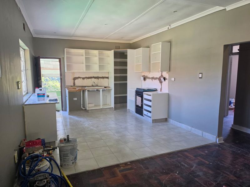 An unfinished kitchen area featuring tiled flooring, built-in cabinetry, and a freestanding stove, currently undergoing renovation with exposed wall sections.