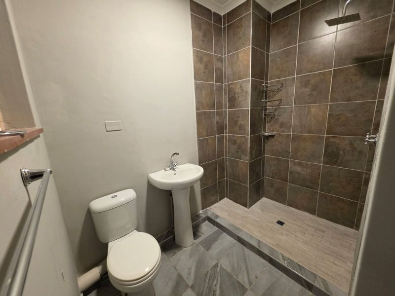 A functional bathroom featuring a pedestal basin, toilet, and a walk-in shower with tiled walls and a rainfall shower head.
