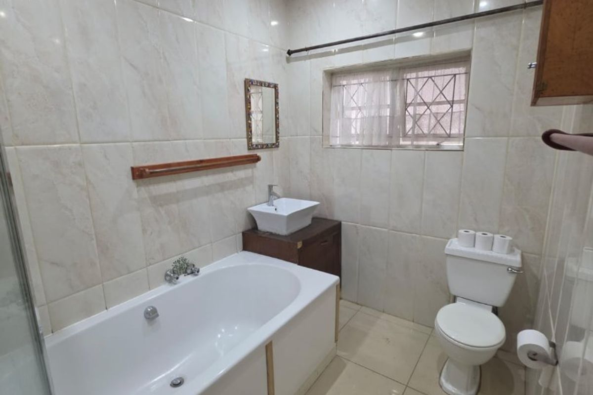 A functional bathroom featuring a bathtub with shower head, vessel sink vanity, and toilet, finished with neutral wall and floor tiles.