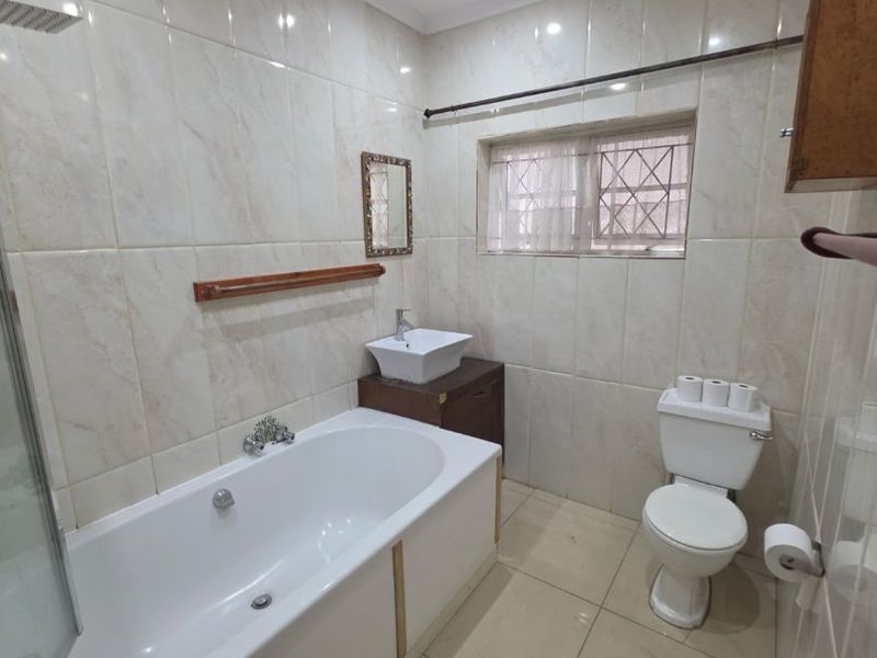 A functional bathroom featuring a bathtub with shower head, vessel sink vanity, and toilet, finished with neutral wall and floor tiles.