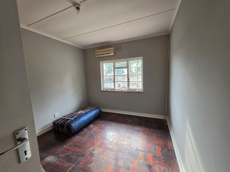 A vacant bedroom featuring original parquet flooring, a wall-mounted air conditioning unit, and security bars on the window.