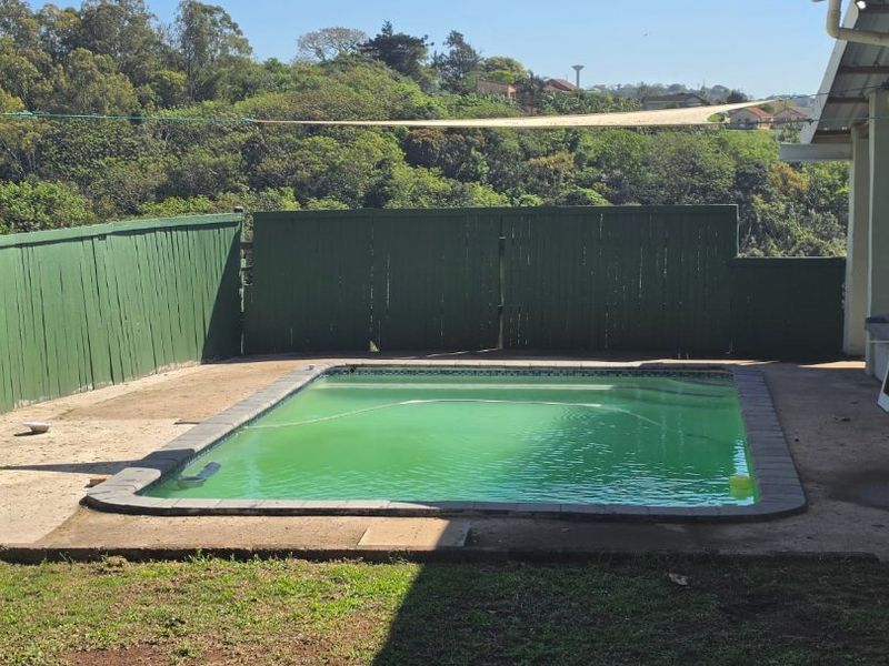 Outdoor pool area featuring a swimming pool, perimeter timber fencing, and concrete paving, set against a natural hillside backdrop.