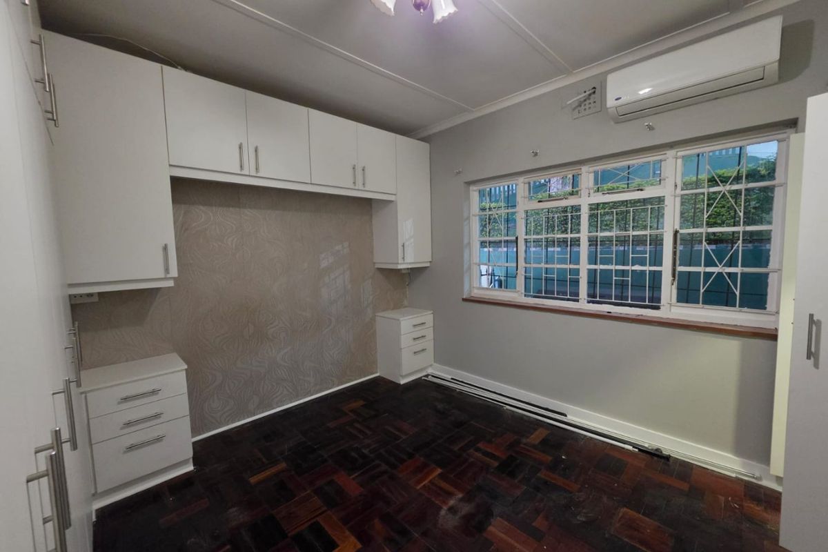 A spacious bedroom featuring built-in cupboards, parquet flooring, and an air conditioning unit, offering a clean and functional space ready for personalization.