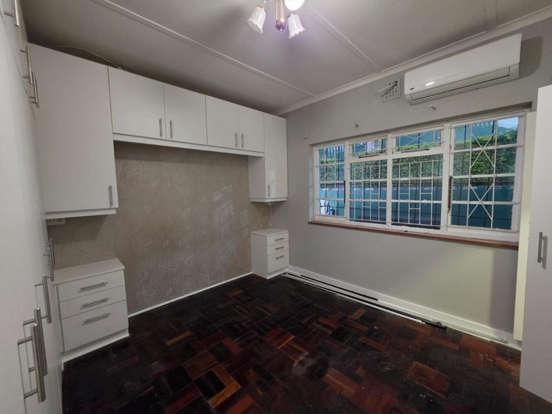A spacious bedroom featuring built-in cupboards, parquet flooring, and an air conditioning unit, offering a clean and functional space ready for personalization.