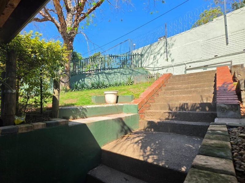 Rear exterior view featuring concrete stairs leading to a terraced garden area with brick retaining walls and security fencing.