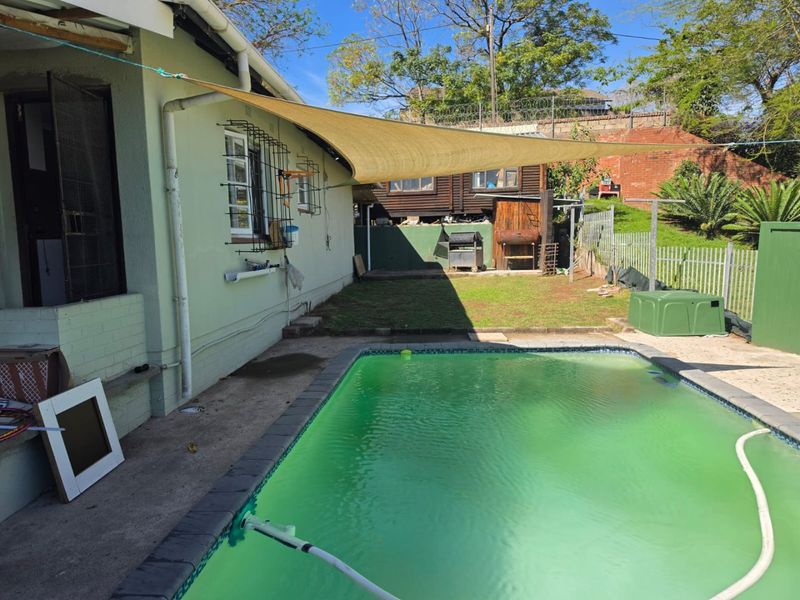Outdoor pool area featuring a shade sail, perimeter fencing, and a swimming pool requiring maintenance.