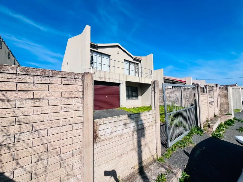 Front exterior view of a two-story townhouse featuring a brick boundary wall, metal gate, paved driveway, and a roller garage door.