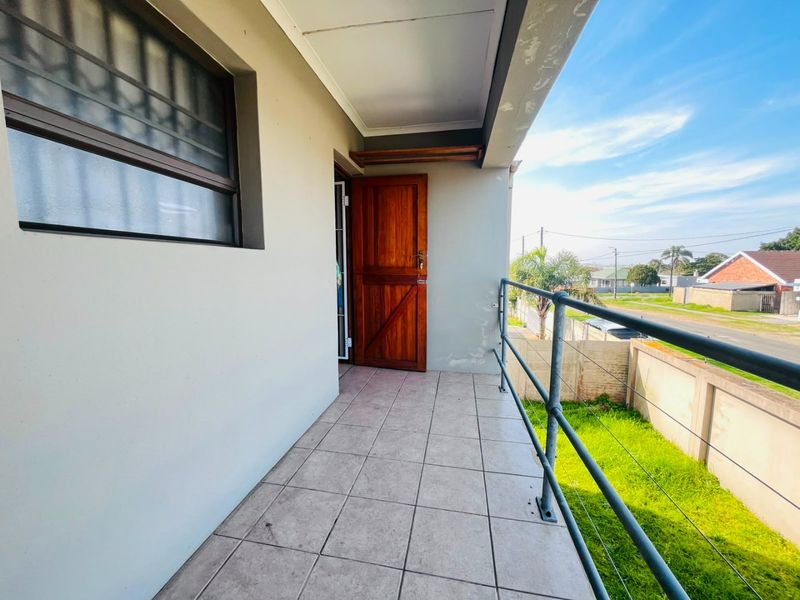 A covered balcony featuring tiled flooring, a timber door, and metal safety railings, overlooking the front garden area.