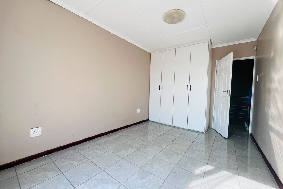 A vacant bedroom featuring tiled flooring, neutral wall paint, and built-in white cupboards, offering a clean canvas for personalization.