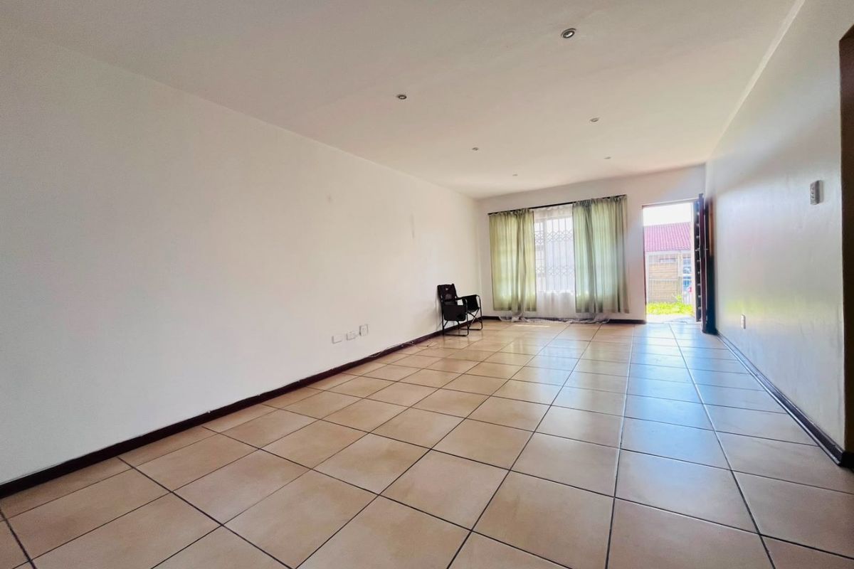 A spacious, empty living area featuring neutral tiled flooring, recessed lighting, and direct access to the exterior through a security gate.