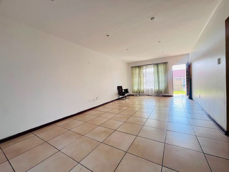 A spacious, empty living area featuring neutral tiled flooring, recessed lighting, and direct access to the exterior through a security gate.