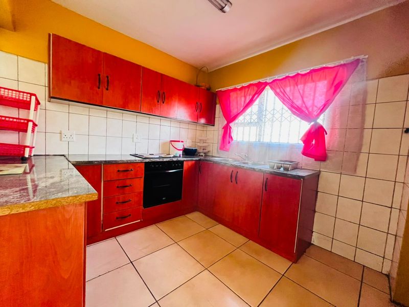 A functional kitchen featuring wood-finish cabinetry, laminate countertops, built-in oven and hob, tiled backsplash, and tiled flooring.
