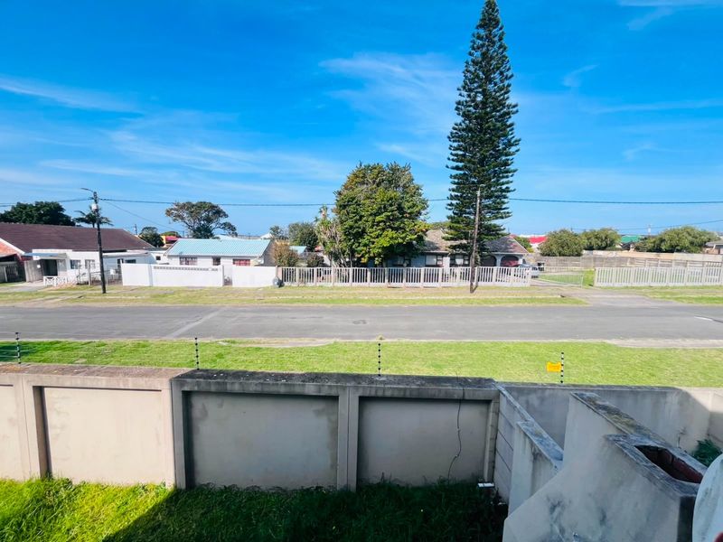 A street-level view showing the property's perimeter wall with electric fencing, facing a residential road and neighboring properties.