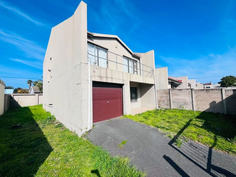 Front view of a two-story residential property featuring a single garage, an upper-level balcony, and a paved driveway with surrounding boundary walls.