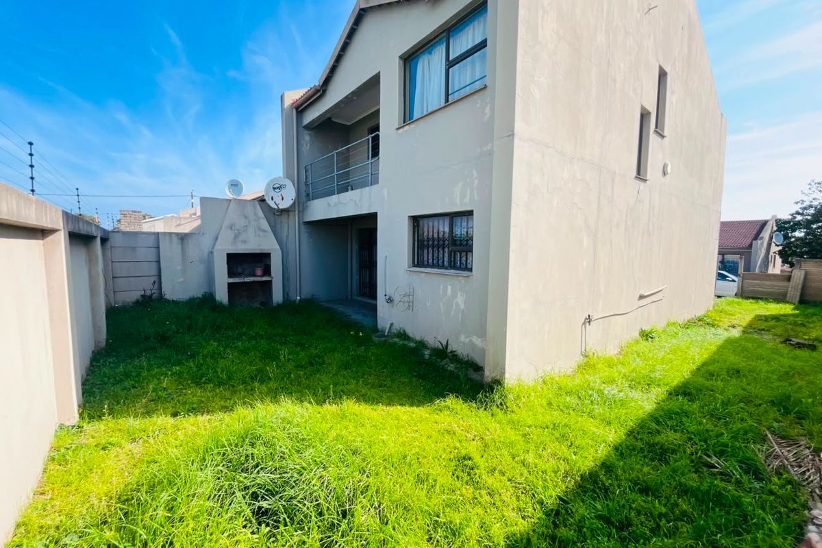 Rear view of the property featuring a small garden, built-in braai area, and an upper-level balcony with security bars on windows.