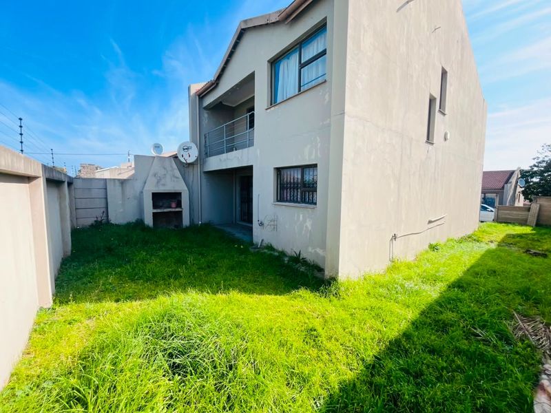 Rear view of the property featuring a small garden, built-in braai area, and an upper-level balcony with security bars on windows.