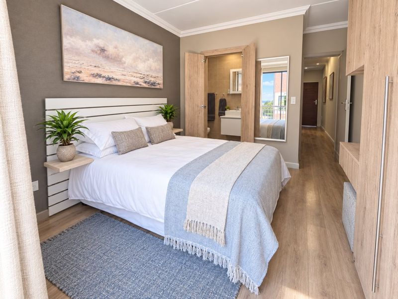 A well-appointed bedroom featuring laminate flooring, a built-in headboard, and an en-suite bathroom with modern finishes.